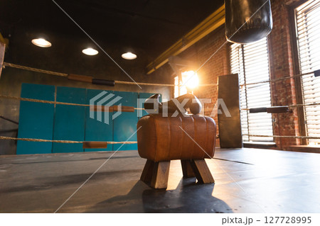 Boxing gloves lying down on boxing ring in empty gym. Equipment for fight training competition black protective boxing gloves ready for fighter winner on ring. Strength fit body workout training 127728995