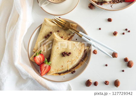 Crepes with chocolate hazelnut spread, strawberries and hazelnuts on a white wooden table. Top view Crepes with chocolate hazelnut spread, strawberries and hazelnuts on a white wooden table. Top view 127729342