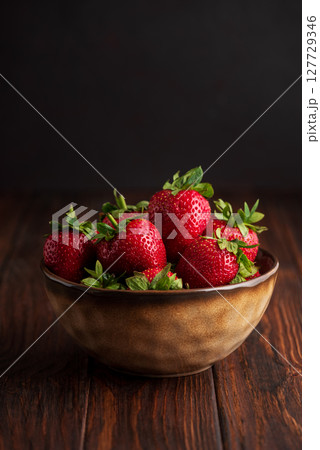 Fresh red strawberries in a rustic bowl on a dark wooden background. Front view Fresh red strawberries in a rustic bowl on a dark wooden background. Front view 127729346