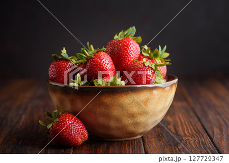 Fresh red strawberries in a rustic bowl on a dark wooden background. Front view Fresh red strawberries in a rustic bowl on a dark wooden background. Front view 127729347