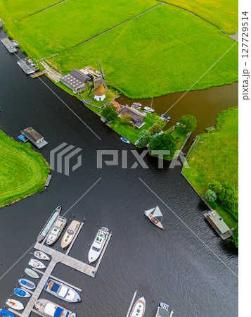 A top-down view of a marina with multiple boats docked along wooden piers, a boat cruising through a narrow waterway surrounded by green parks and natural grassy areas. 127729514