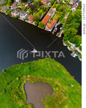 A top-down view of a marina with multiple boats docked along wooden piers, a boat cruising through a narrow waterway surrounded by green parks and natural grassy areas. A top-down view of a marina with multiple boats docked along wooden piers, a boat cruising through a narrow waterway surrounded by green parks and natural grassy areas. 127729522