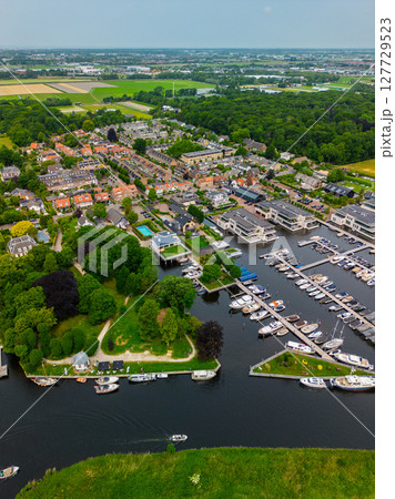 A top-down view of a marina with multiple boats docked along wooden piers, a boat cruising through a narrow waterway surrounded by green parks and natural grassy areas. A top-down view of a marina with multiple boats docked along wooden piers, a boat cruising through a narrow waterway surrounded by green parks and natural grassy areas. 127729523