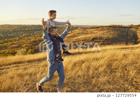 Portrait of little child boy sitting on fathers shoulders enjoying sunset and nature outdoors. 127729554