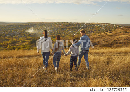 Family with children is walking on golden hill in middle of picturesque landscape. 127729555