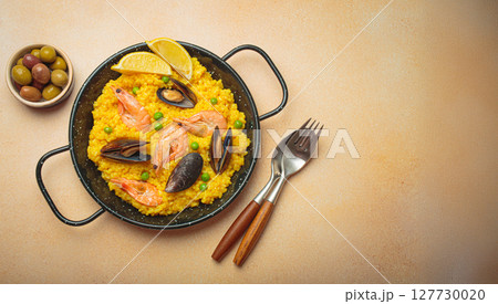 Spanish seafood Paella with shrimps, mussels, peas and lemon in a pan on light beige background top view 127730020
