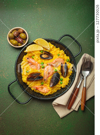 Spanish seafood Paella with shrimps, mussels, peas and lemon in a pan on green rustic background top view Spanish seafood Paella with shrimps, mussels, peas and lemon in a pan on green rustic background top view 127730026