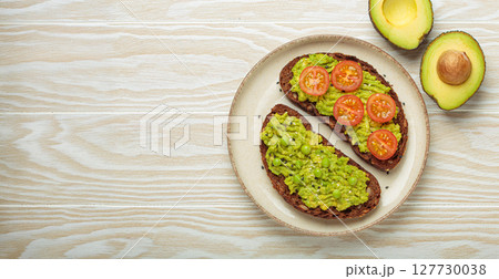 Healthy avocado toast with green peas and cherry tomatoes on whole rye bread top view on white wooden background 127730038