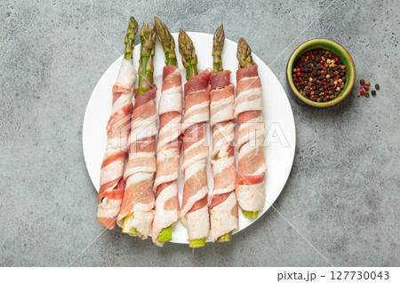 Fresh asparagus wrapped in bacon with peppercorns on gray concrete background top view Fresh asparagus wrapped in bacon with peppercorns on gray concrete background top view 127730043