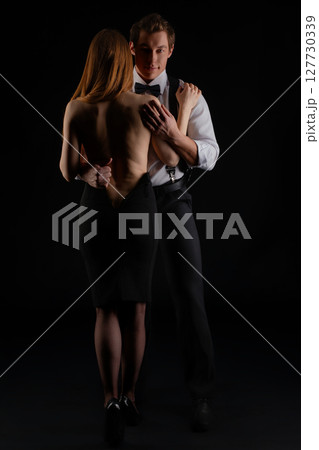 Couple dancing elegantly in a dramatic setting with black background Couple dancing elegantly in a dramatic setting with black background 127730339