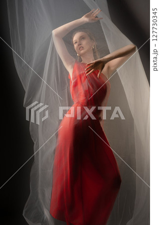 Dynamic woman expressing emotion in elegant red dress with soft drapery in a studio setting Dynamic woman expressing emotion in elegant red dress with soft drapery in a studio setting 127730345