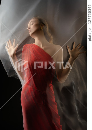 Captivating woman expresses emotion in studio setting while posing with flowing fabric Captivating woman expresses emotion in studio setting while posing with flowing fabric 127730346