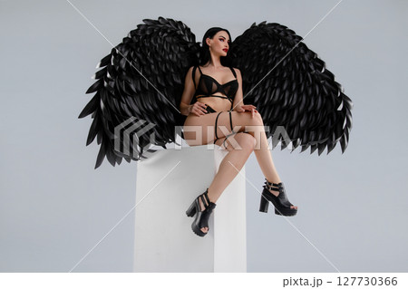 Woman in black lingerie with striking wings posed gracefully on a pedestal 127730366
