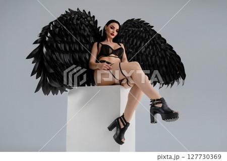 Elegant woman in lingerie poses with striking black wings in a stylish setting 127730369