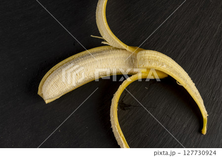 one open yellow banana on a black slate board, ripe and sweet yellow banana on a kitchen board made of black stone 127730924
