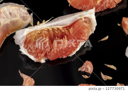 red citrus fruit on the table, peeled citrus grapefruit with bright red and juicy flesh, the fruit is reflected on a black mirror surface red citrus fruit on the table, peeled citrus grapefruit with bright red and juicy flesh, the fruit is reflected on a black mirror surface 127730971