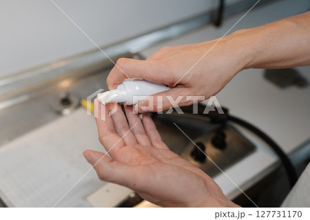 Close-up cropped shot of unrecognizable man pouring cleaning foam from bottle while standing in kitchen near dirty gas stove, preparing to tackle dirt and grime. Concept of cleaning and household. 127731170