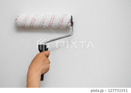 Female arm holding a paint roller against a plain white wall, DIY renovation concept Female arm holding a paint roller against a plain white wall, DIY renovation concept 127731551