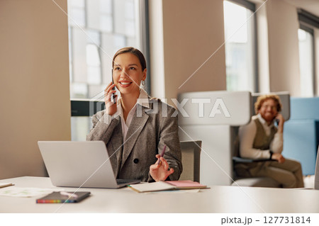 A Professional Woman Working in an Office, Engaging on Both Her Phone and Laptop Efficiently 127731814