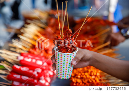 Filipino street food in takeaway paper cup with grilled chicken intestines on skewers, ideal for food delivery, travel blogs, or menu design 127732436