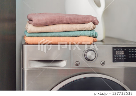 Stack of soft muslin baby swaddles neatly folded on a modern washing machine in a bright laundry room. Concept of baby care, hygiene, and gentle fabric for newborn essentials Stack of soft muslin baby swaddles neatly folded on a modern washing machine in a bright laundry room. Concept of baby care, hygiene, and gentle fabric for newborn essentials 127732535