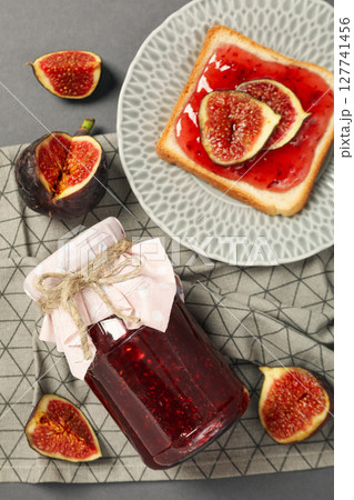 Figs, jars of jam, towel and bread with jam on plate on gray background, top view 127741456