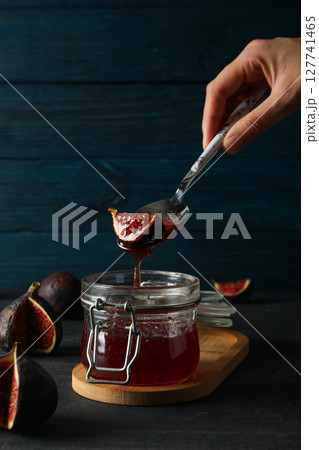 Jar of jam and spoon with figs in hand on blue wooden background Jar of jam and spoon with figs in hand on blue wooden background 127741465