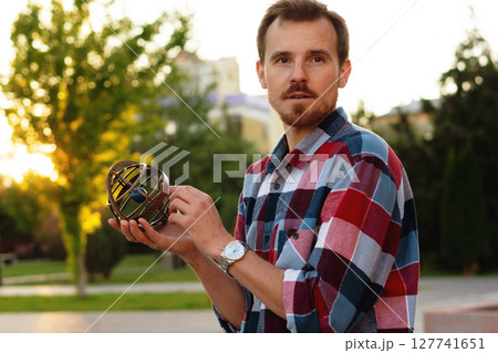 Young man holding antique globe thoughtfully during sunset outdoors 127741651