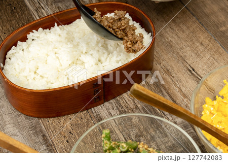 三食丼弁当を詰める そぼろ,いんげんの胡麻和え, 炒り卵をご飯に乗せる 127742083