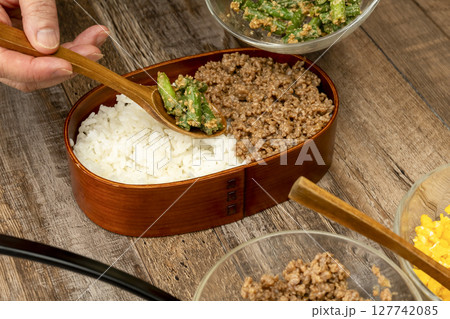 三食丼弁当を詰める そぼろ,いんげんの胡麻和え, 炒り卵をご飯に乗せる 三食丼弁当を詰める そぼろ,いんげんの胡麻和え, 炒り卵をご飯に乗せる 127742085