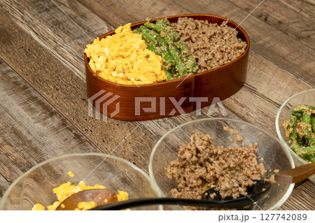 三食丼弁当を詰める そぼろ,いんげんの胡麻和え, 炒り卵をご飯に乗せる 三食丼弁当を詰める そぼろ,いんげんの胡麻和え, 炒り卵をご飯に乗せる 127742089