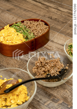 三食丼弁当を詰める そぼろ,いんげんの胡麻和え, 炒り卵をご飯に乗せる 127742090