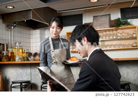飲食店で男性客に食事の配膳をする女性店員 飲食店で男性客に食事の配膳をする女性店員 127742623
