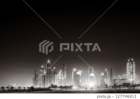 Urban city skyline with illuminated skyscrapers and waterfront railing in black and white at night, Dubai Marina bay UAE 127746811