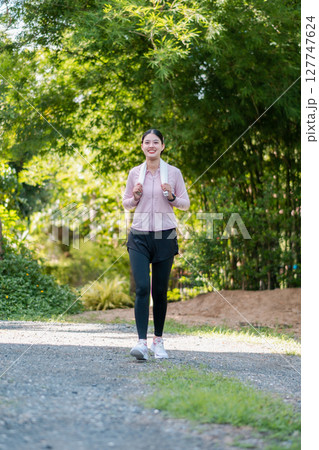 A woman in athletic wear walking on a path surrounded by greenery, enjoying a peaceful morning in the park. 127747624