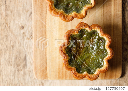 Closeup of Matcha and mochi Portuguese sweet dessert egg tart or Pastel de Nata on wooden board on wooden table. Closeup of Matcha and mochi Portuguese sweet dessert egg tart or Pastel de Nata on wooden board on wooden table. 127750407