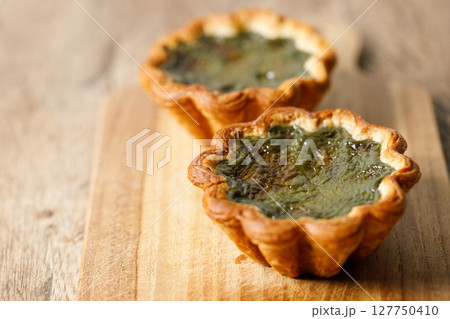 Closeup of Matcha and mochi Portuguese sweet dessert egg tart or Pastel de Nata on wooden board on wooden table. Closeup of Matcha and mochi Portuguese sweet dessert egg tart or Pastel de Nata on wooden board on wooden table. 127750410