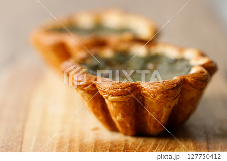 Closeup of Matcha and mochi Portuguese sweet dessert egg tart or Pastel de Nata on wooden board on wooden table. 127750412