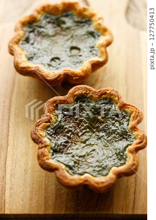 Closeup of Matcha and mochi Portuguese sweet dessert egg tart or Pastel de Nata on wooden board on wooden table. Closeup of Matcha and mochi Portuguese sweet dessert egg tart or Pastel de Nata on wooden board on wooden table. 127750413