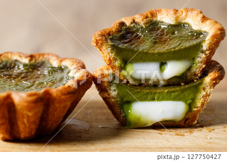 Closeup of Matcha and mochi Portuguese sweet dessert egg tart or Pastel de Nata on wooden board on wooden table. 127750427