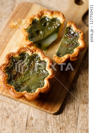 Closeup of Matcha and mochi Portuguese sweet dessert egg tart or Pastel de Nata on wooden board on wooden table. 127750431