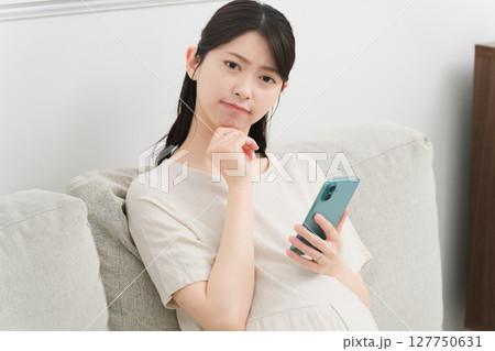 ソファーでスマートフォンを操作する妊婦　ライフスタイルイメージ 127750631