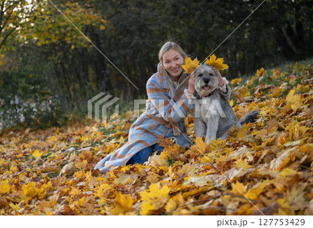 Smiling woman playing with her dog in autumn park with colorful fallen leaves Smiling woman playing with her dog in autumn park with colorful fallen leaves 127753429