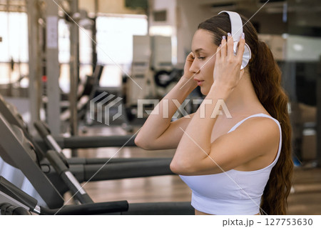 Young sporty woman running on machine in the gym and listening music in headphones 127753630