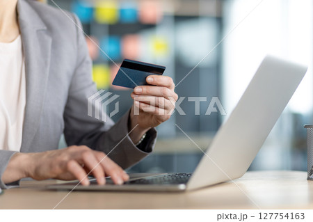 A woman is shopping online using her credit card and laptop in the office, making secure purchases from the comfort of her desk A woman is shopping online using her credit card and laptop in the office, making secure purchases from the comfort of her desk 127754163