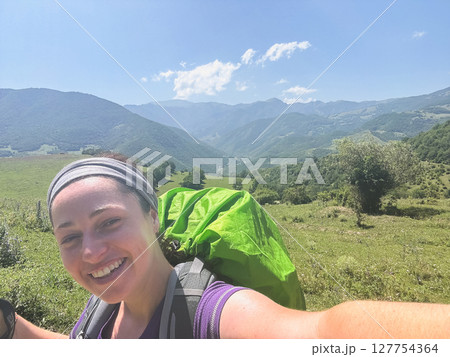 Hiking tourism adventure. Backpacker hiker woman taking selfie picture. Hiker girl lady tourist with backpack walking near mountain. Young happy woman enjoy hike trekking tourism active vacation 127754364