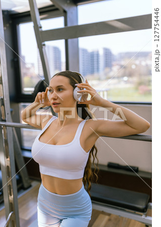 Sexy girl wearing sportswear is posing next smith machine in the fitness center. Sexy girl wearing sportswear is posing next smith machine in the fitness center. 127754446