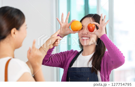 Healthy Lifestyle and Fun Cooking. Two women enjoying playful moments with fruits in a bright kitchen. 127754795