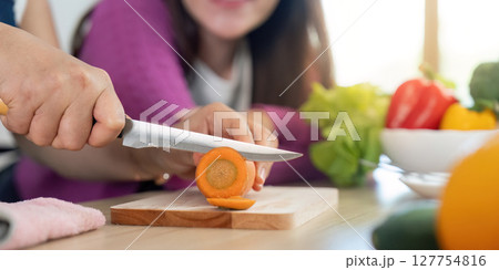 Chopping Fresh Vegetables. Close-up of a woman slicing a carrot while another woman observes. Chopping Fresh Vegetables. Close-up of a woman slicing a carrot while another woman observes. 127754816