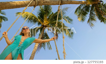 Seductive woman swinging on a swing on a tropical beach, on shores of the turquoise sea. Concept travel, walks, rest in sea, tropical resort coastline relaxation traveling tourism summer holidays. 127755193